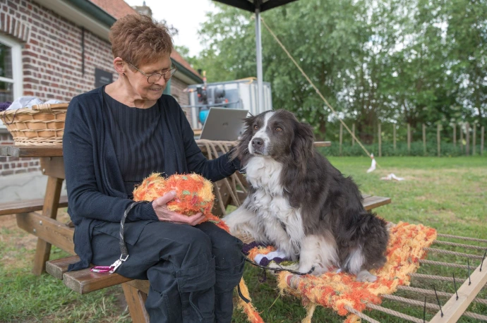 Vrijwilligster uit het wolatelier maakt een hangmat waar een hond op zit